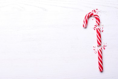 Photo of Broken sweet Christmas candy cane on white wooden table, top view. Space for text