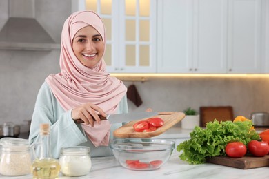 Muslim woman making delicious salad with vegetables at white table in kitchen. Space for text