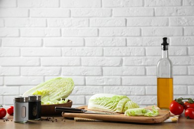 Cut fresh Chinese cabbage, tomatoes, oil and spices on wooden table near white brick wall