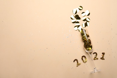 Photo of Year number 2021, glass and shiny confetti on beige background, flat lay. Space for text