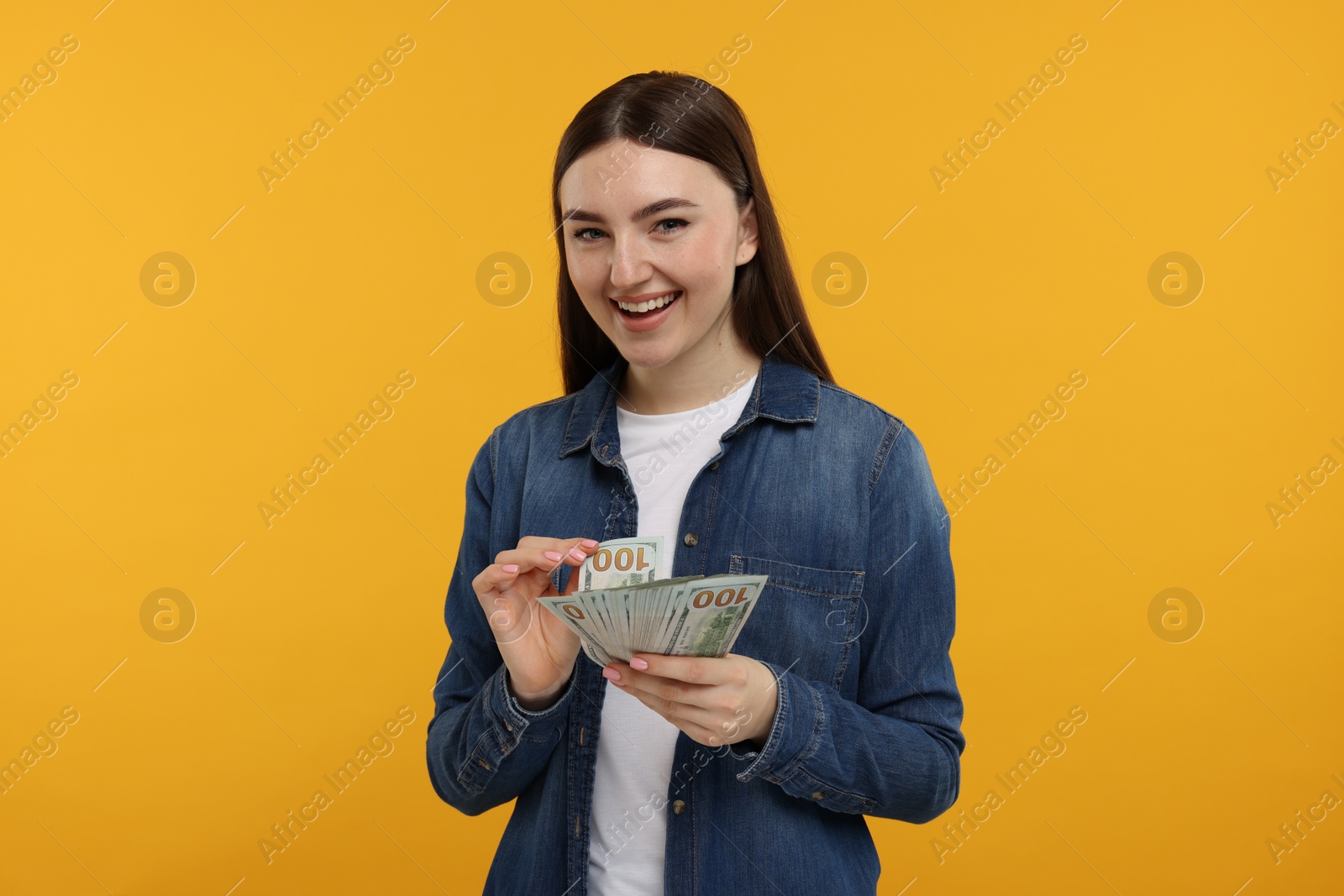 Photo of Happy woman with dollar banknotes on orange background