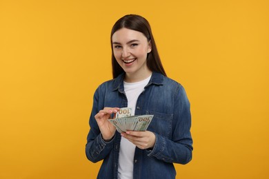 Photo of Happy woman with dollar banknotes on orange background