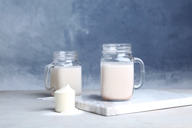 Photo of Mason jars with protein shake and scoop of powder on table