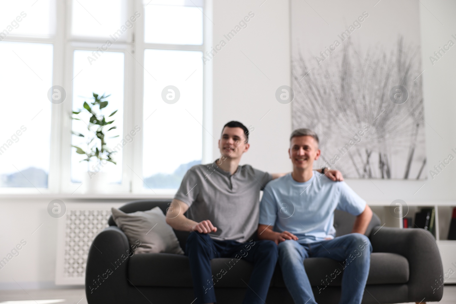 Photo of Blurred view of happy men sitting on sofa at home