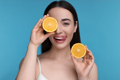 Photo of Beautiful young woman with pieces of orange on light blue background