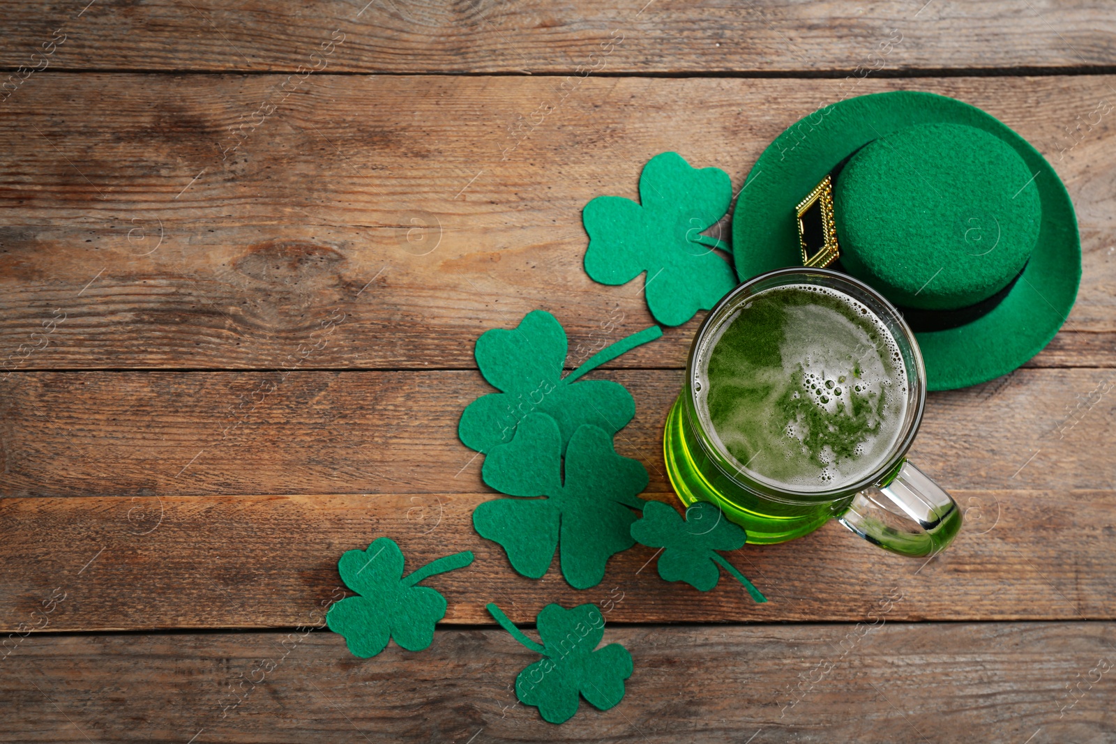 Photo of Green beer, hat and clover leaves on wooden table, flat lay with space for text. St. Patrick's Day celebration