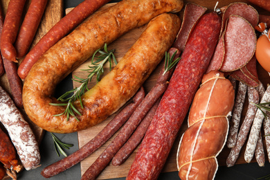 Different tasty sausages on black table, flat lay