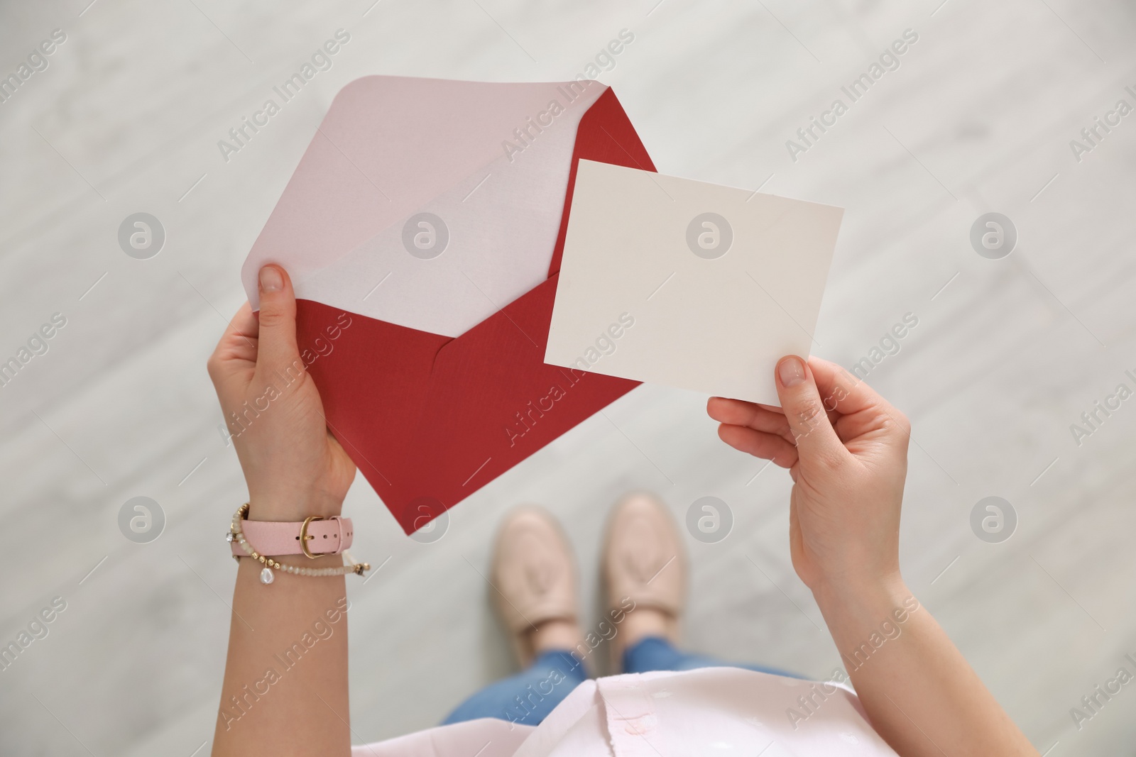 Photo of Woman holding envelope and blank greeting card indoors, top view