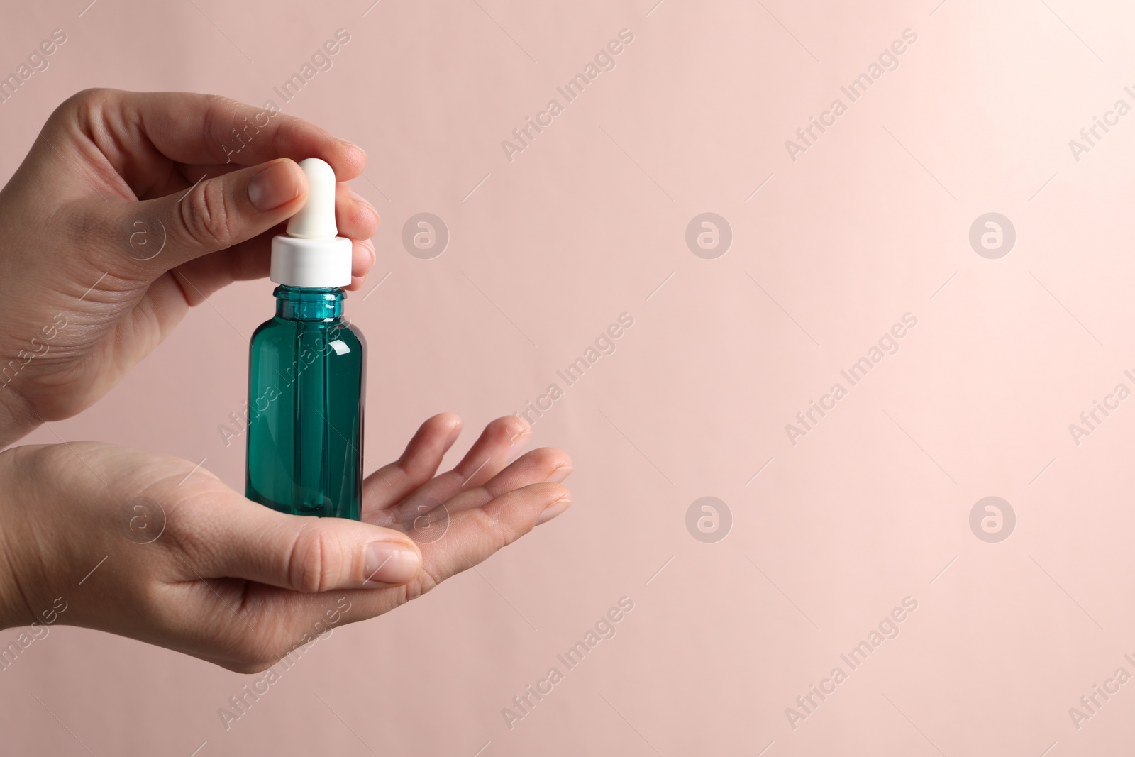 Photo of Woman with bottle of cosmetic serum on light pink background, closeup. Space for text