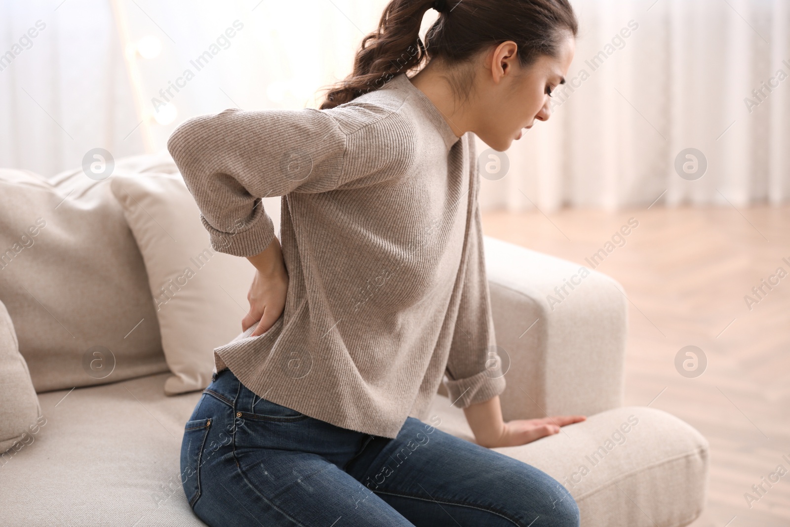 Photo of Woman suffering from back pain at home. Bad posture problem