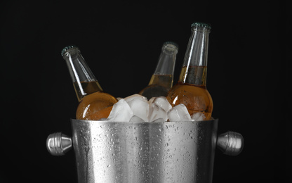 Metal bucket with bottles of beer and ice cubes on black background