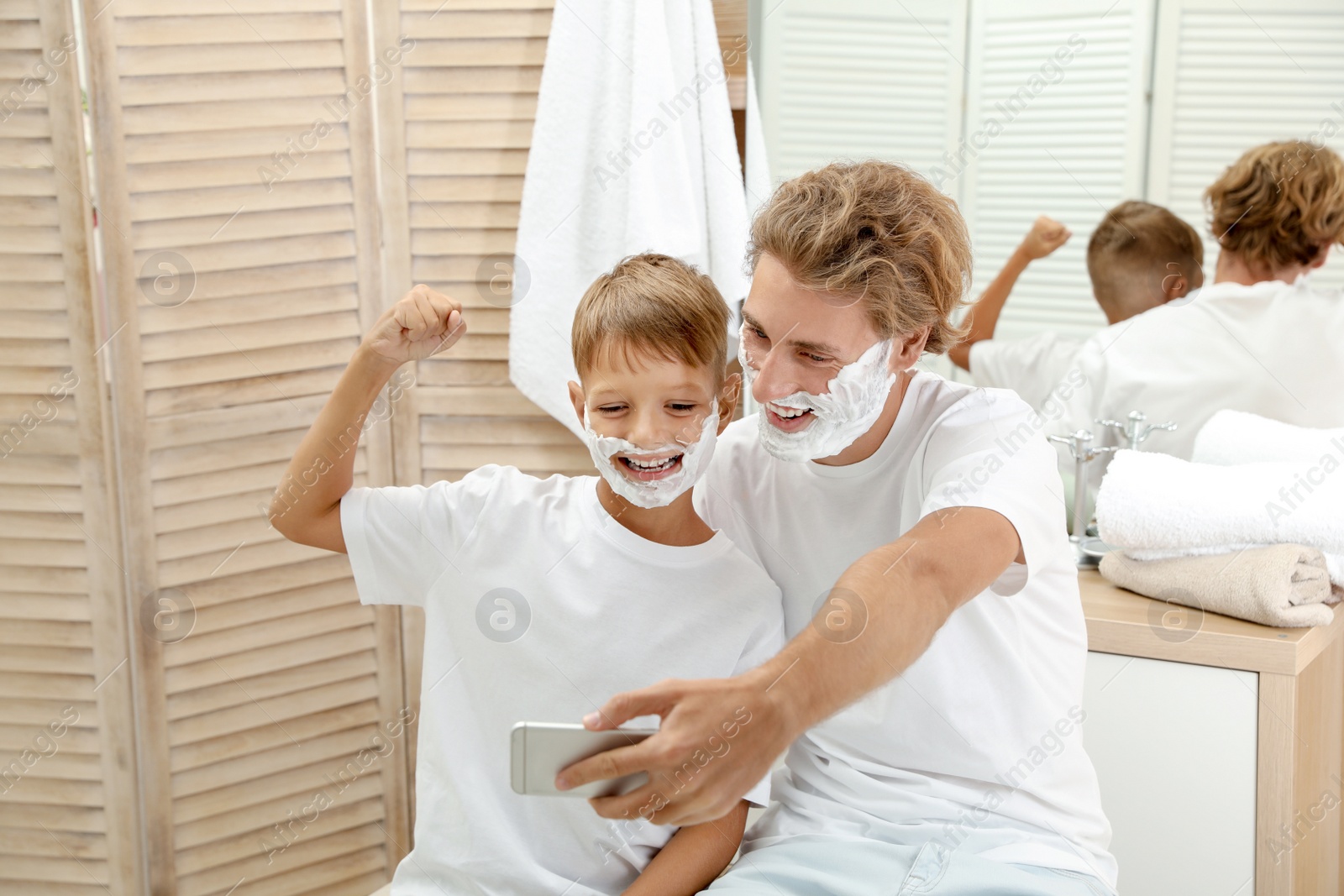 Photo of Father and son taking selfie with shaving foam on faces in bathroom