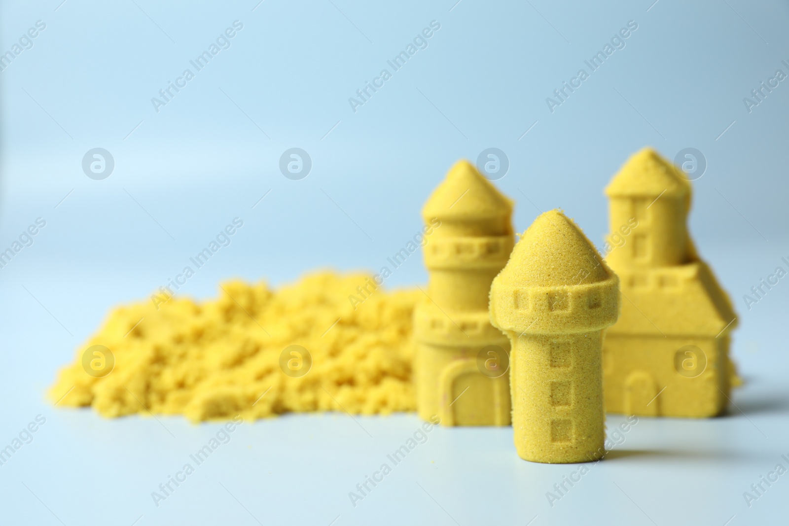 Photo of Castle figures made of yellow kinetic sand on light blue background, closeup. Space for text