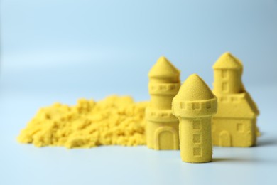 Castle figures made of yellow kinetic sand on light blue background, closeup. Space for text