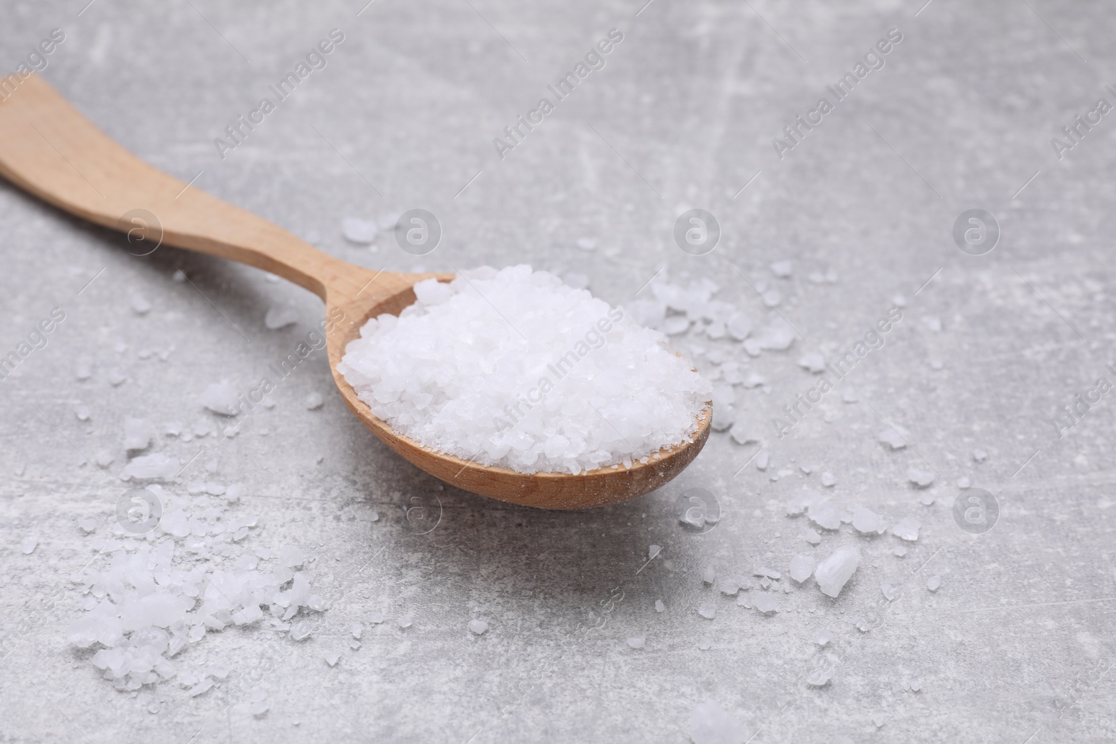 Photo of Spoon with sea salt on light grey table, closeup. Space for text