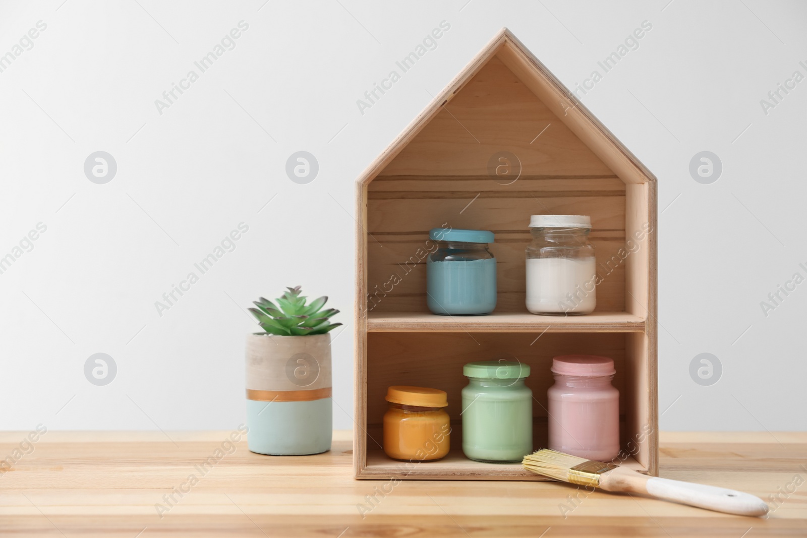 Photo of House shaped shelf and jars of paints on table against white background