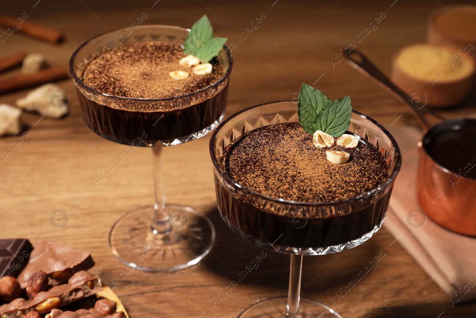 Photo of Dessert bowls of delicious hot chocolate and ingredients on wooden table, closeup