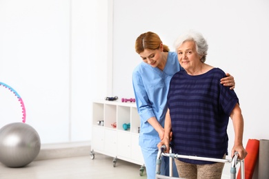 Photo of Caretaker helping elderly woman with walking frame indoors