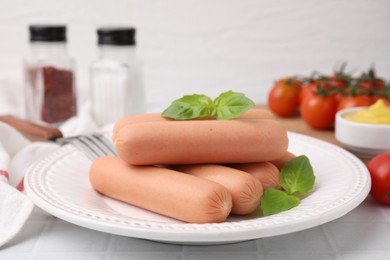 Photo of Delicious boiled sausages and basil on white tiled table