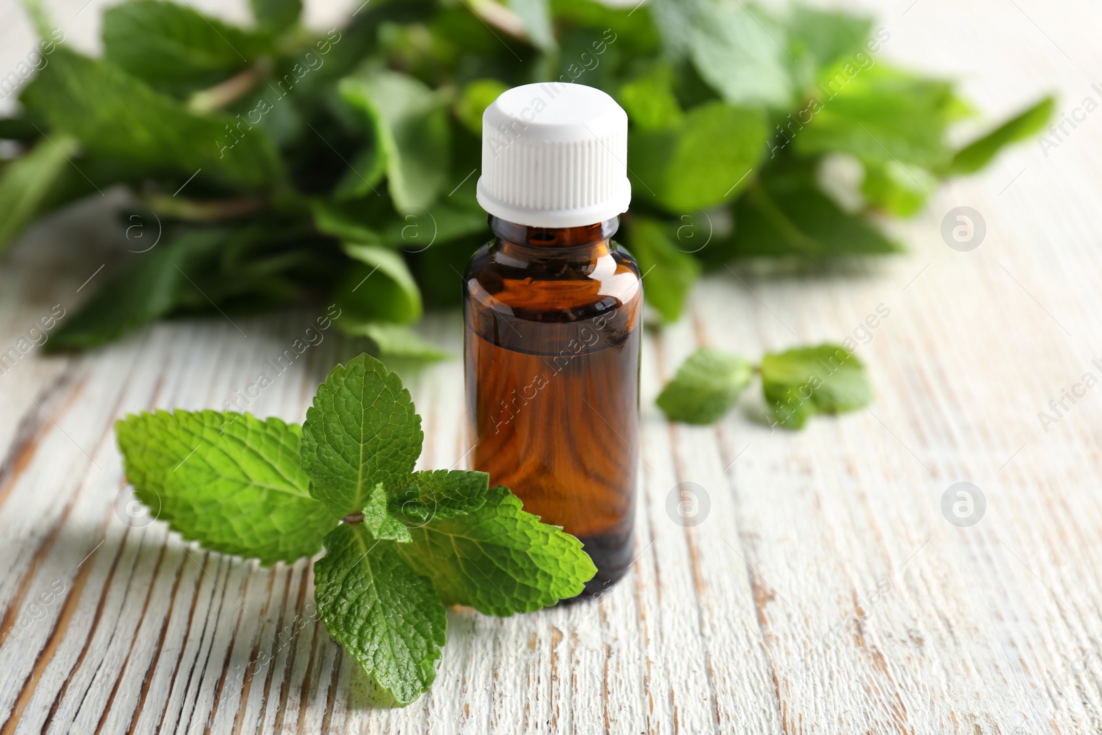 Photo of Bottle of essential oil with mint leaves on wooden table