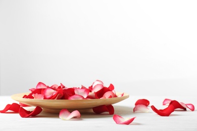 Wooden plate with rose petals on table against white background. Space for text