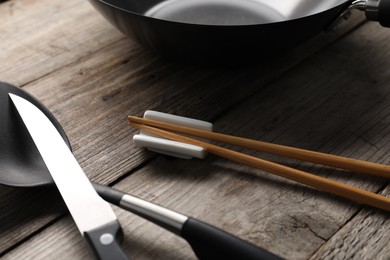 Photo of Black metal wok, chopsticks, knife and spatula on wooden table, closeup