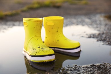 Photo of Yellow rubber boots in puddle outdoors. Autumn walk