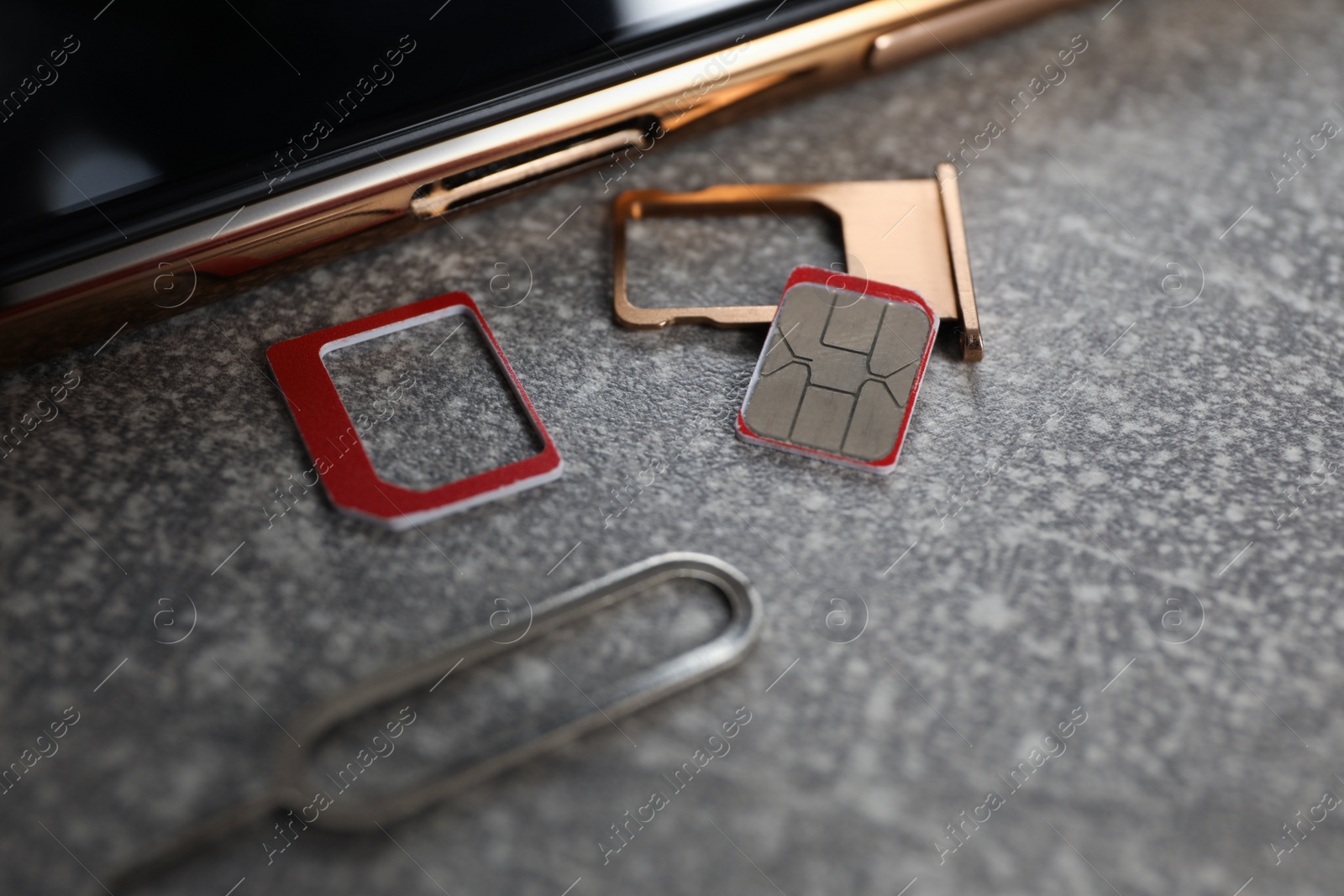 Photo of SIM card, mobile phone, tray and ejector tool on grey table, closeup