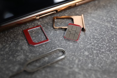 Photo of SIM card, mobile phone, tray and ejector tool on grey table, closeup