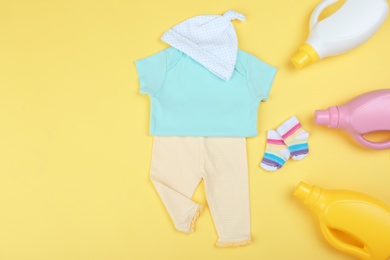 Photo of Flat lay composition with detergents and children's clothes on yellow background. Space for text