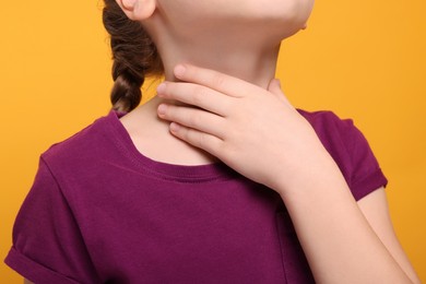 Photo of Girl suffering from sore throat on orange background, closeup