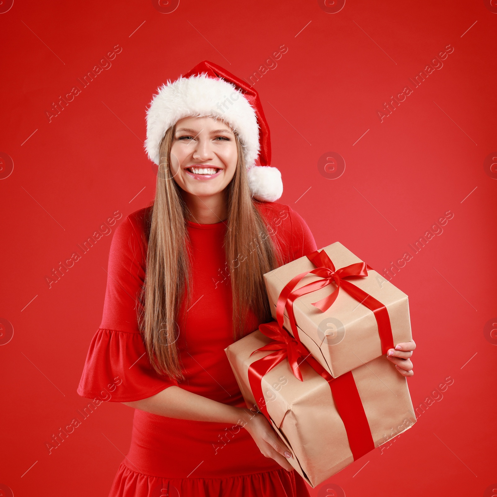 Photo of Happy young woman in Santa hat with Christmas gifts on red background