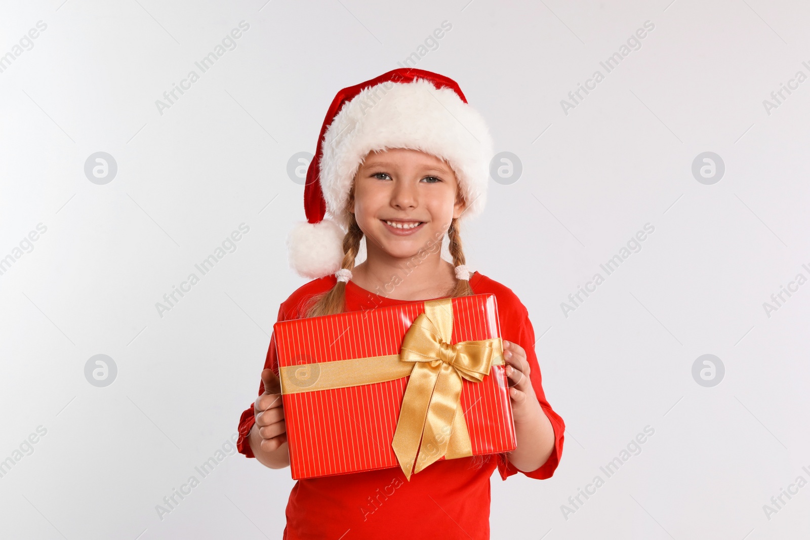 Photo of Happy little child in Santa hat with gift box on light grey background. Christmas celebration