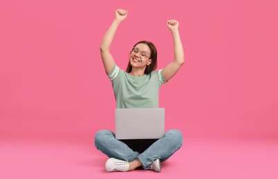 Young woman with modern laptop on pink background