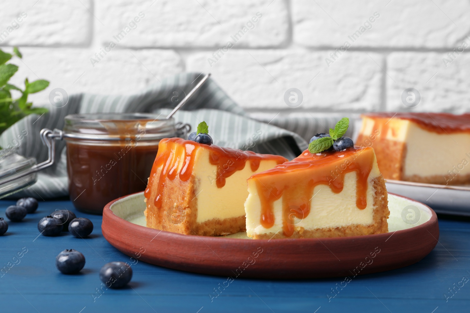 Photo of Pieces of delicious caramel cheesecake with blueberry and mint on blue wooden table