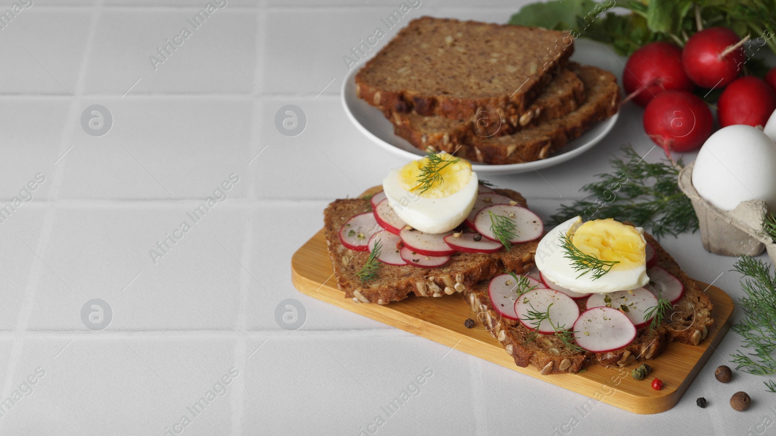 Photo of Tasty sandwiches with boiled egg, radish and ingredients on white tiled table, space for text