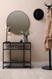 Photo of Console table, clothes rack and mirror on beige wall in hallway. Interior design