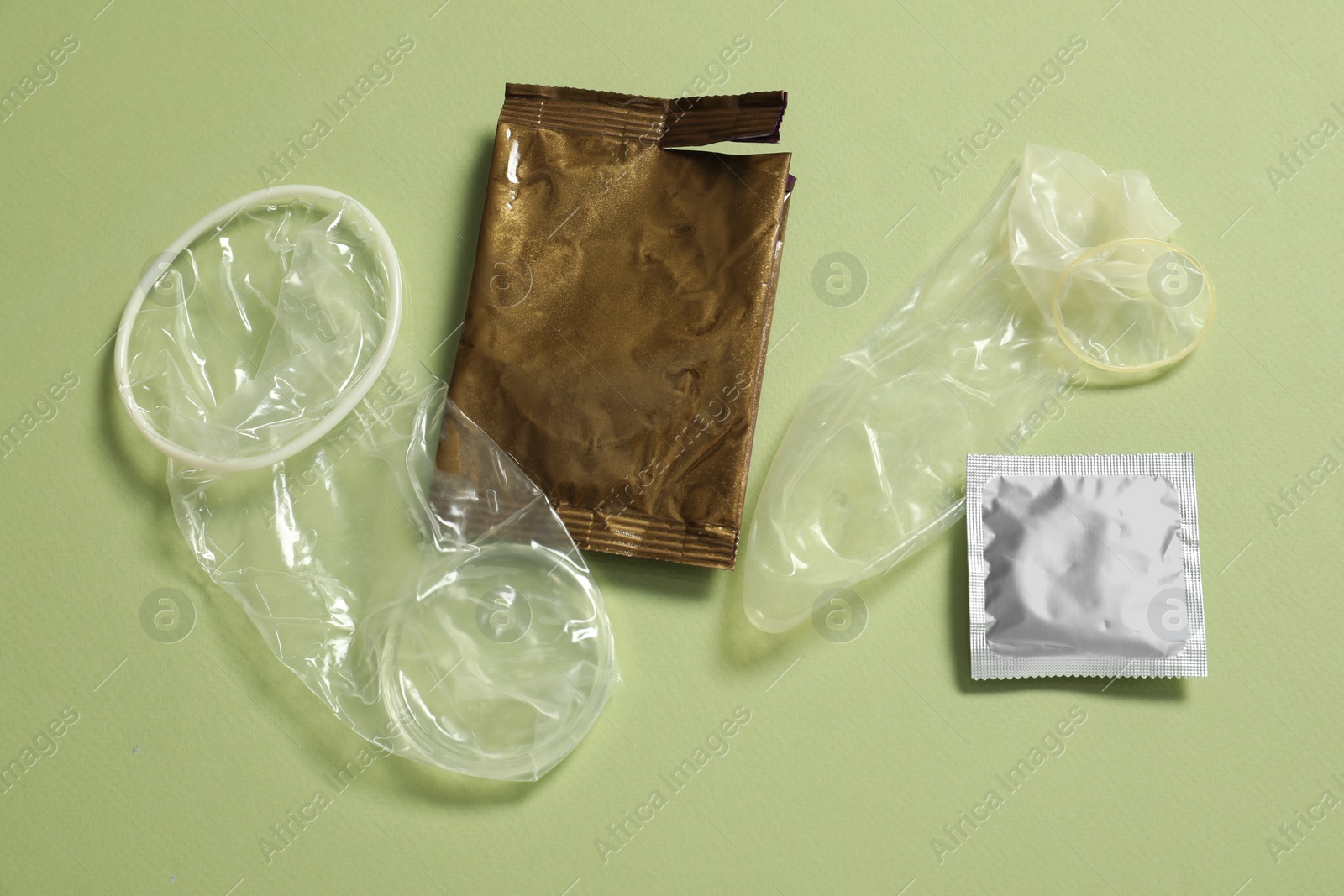 Photo of Unrolled female, male condoms and packages on light green background, flat lay. Safe sex