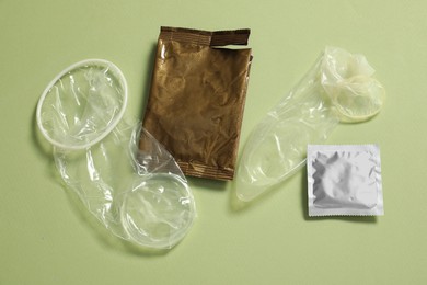Photo of Unrolled female, male condoms and packages on light green background, flat lay. Safe sex