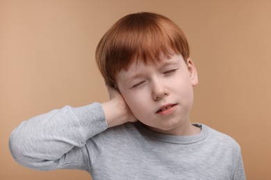 Photo of Hearing problem. Little boy suffering from ear pain on pale brown background