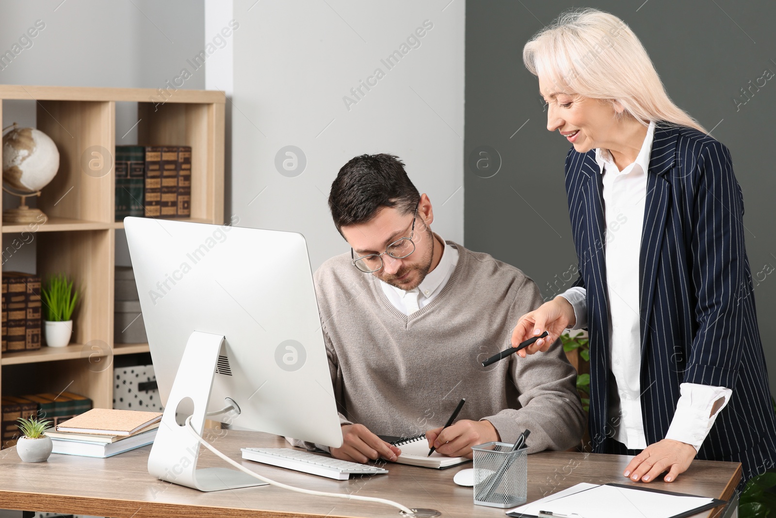 Photo of Boss and employee writing in notebook at wooden table