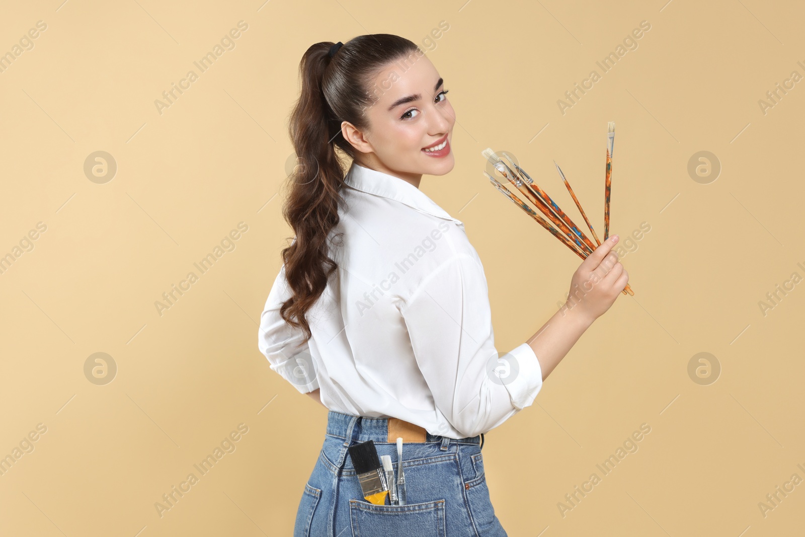 Photo of Woman with paintbrushes on beige background. Young artist