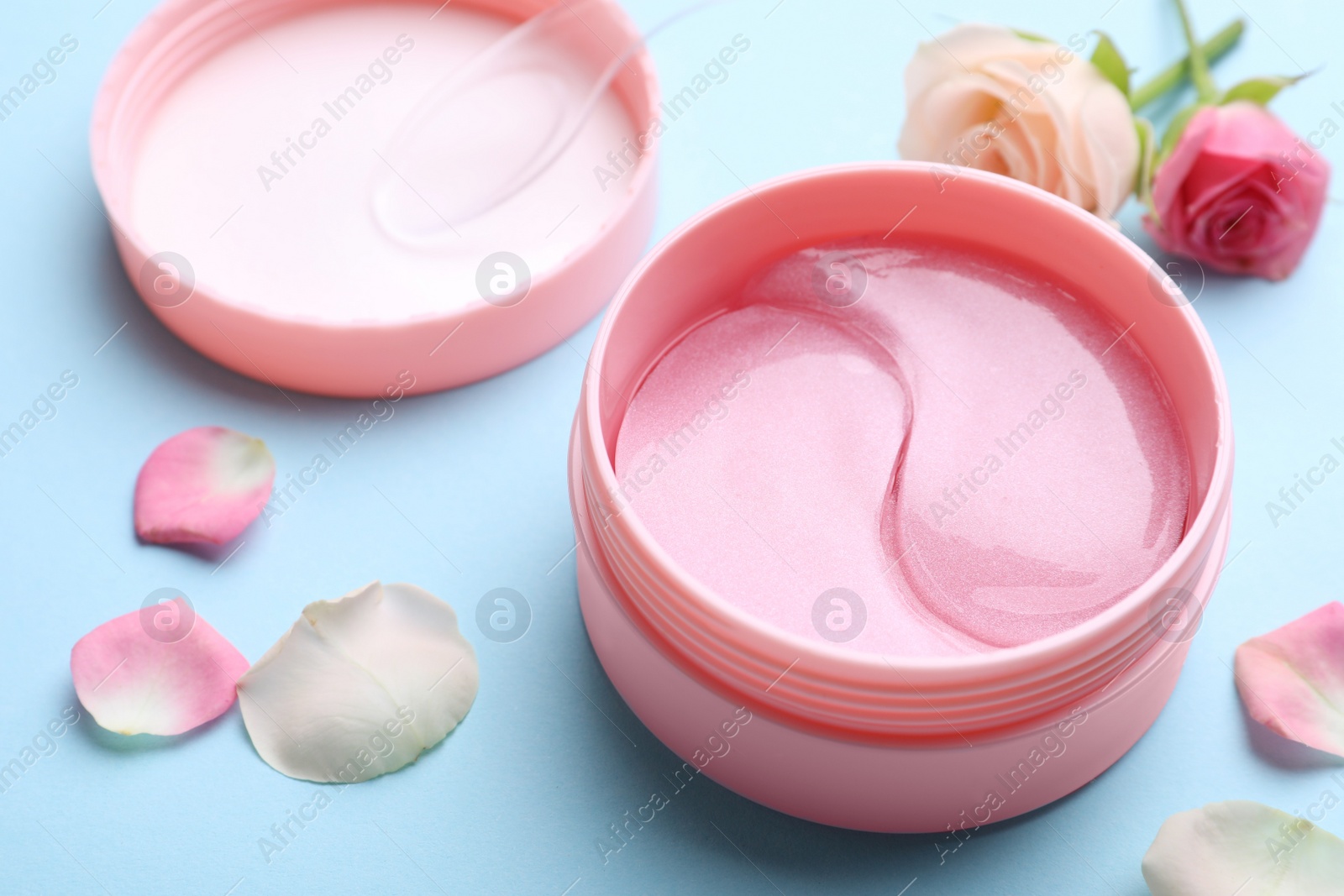 Photo of Under eye patches in jar and rose flowers on light blue background, closeup. Cosmetic product