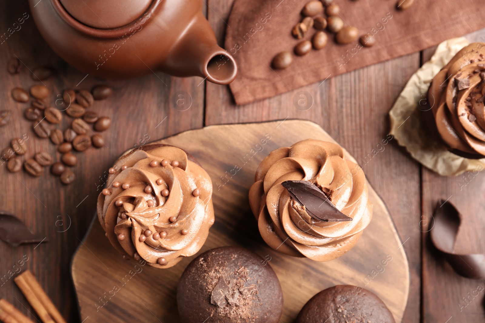 Photo of Delicious chocolate muffins and cupcakes decorated with cream on wooden table, flat lay