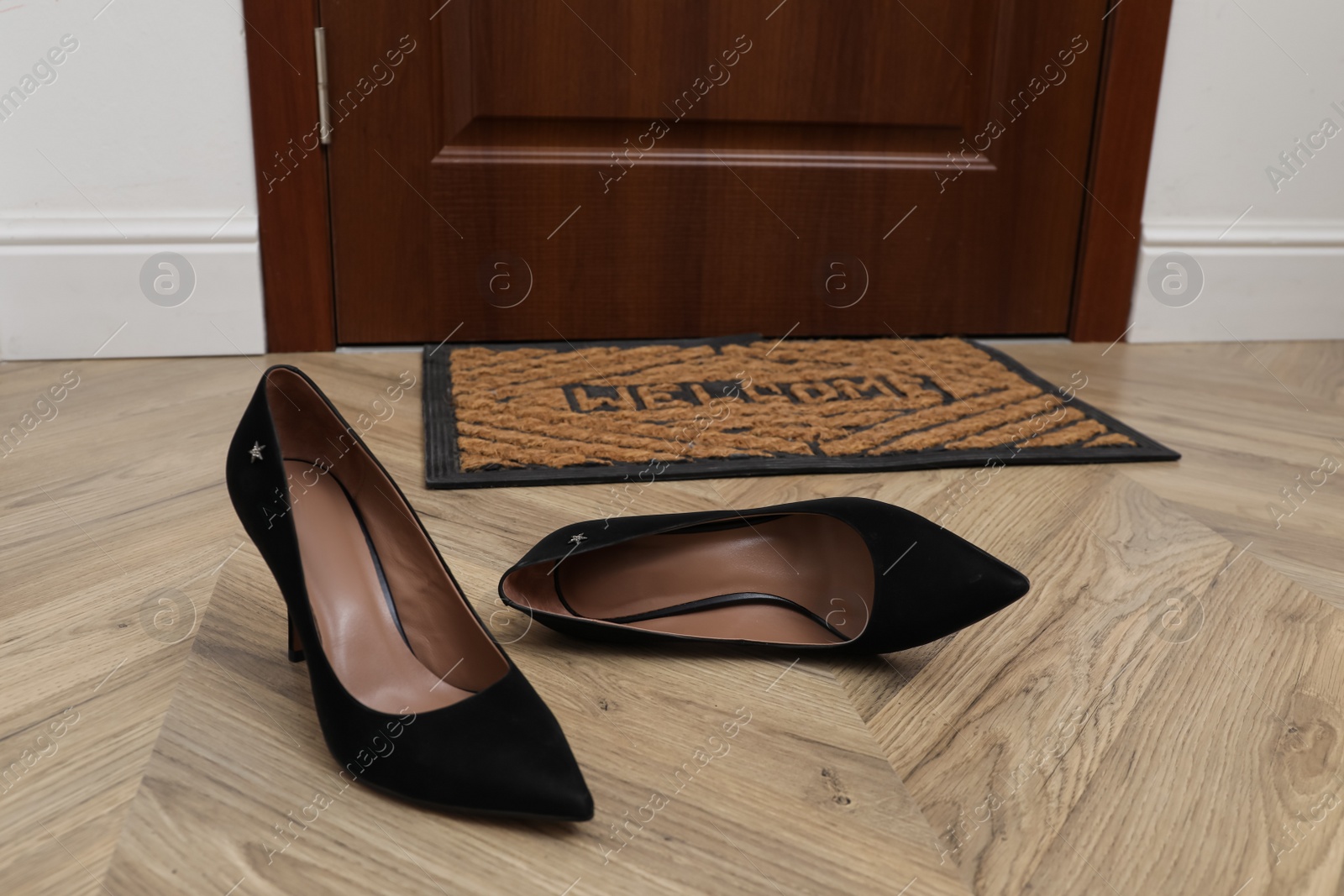 Photo of Stylish female shoes near door mat in hall
