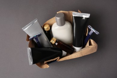 Box with different men's shaving accessories and cosmetics on dark grey background, top view