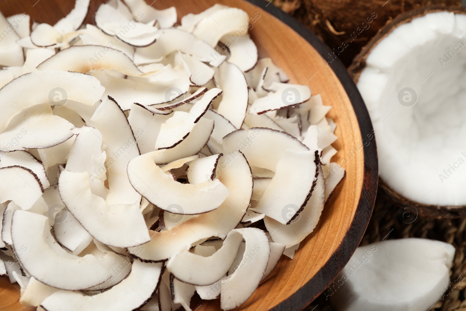 Photo of Tasty coconut chips in wooden bowl, closeup