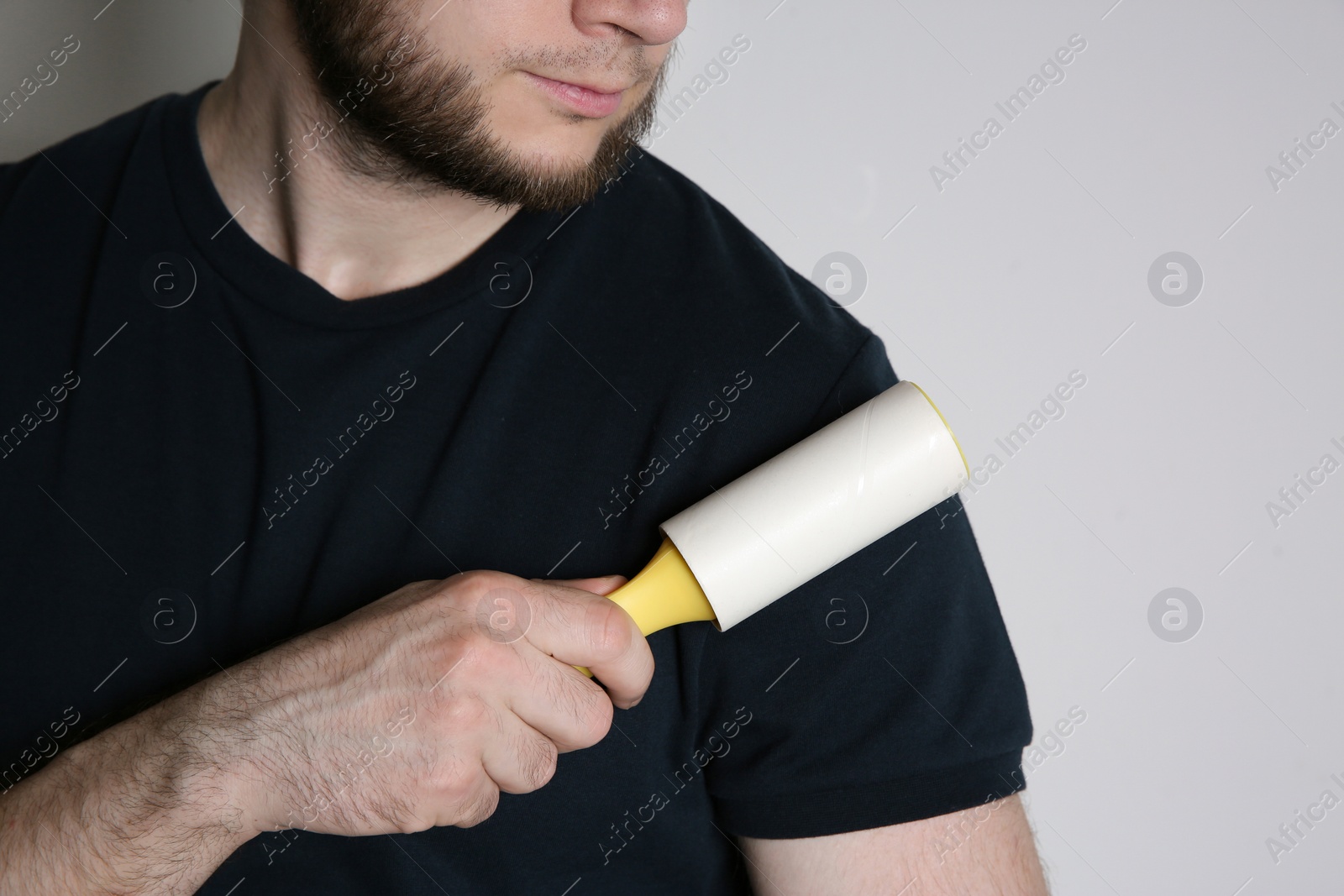 Photo of Man cleaning black t-shirt with lint roller on white background, closeup