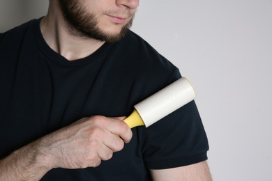 Man cleaning black t-shirt with lint roller on white background, closeup