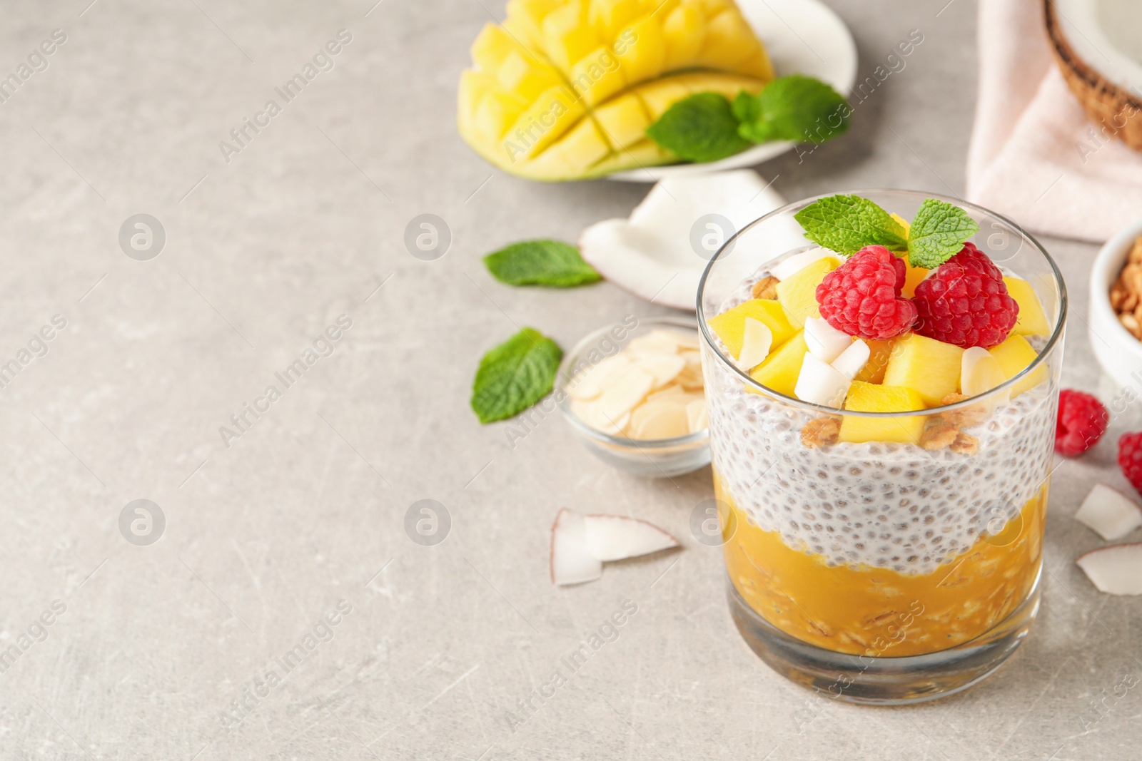 Photo of Delicious chia pudding with mango, raspberries and granola on light grey table, space for text